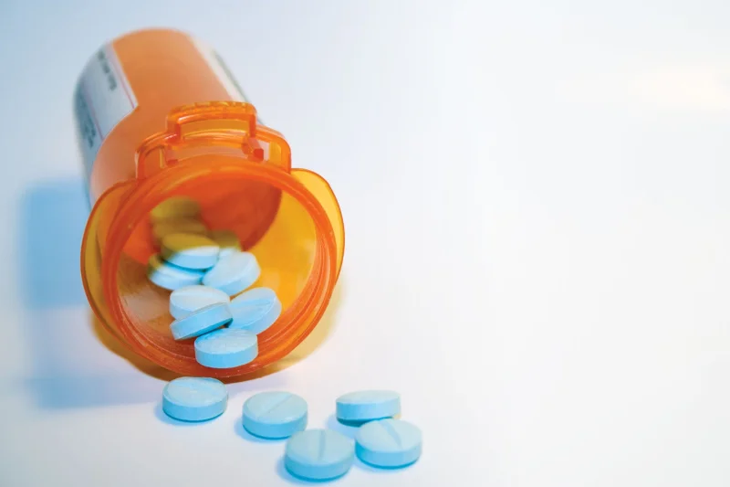 Blue opioid pills spilling from a prescription bottle representing fentanyl and comparison with other opioid medications