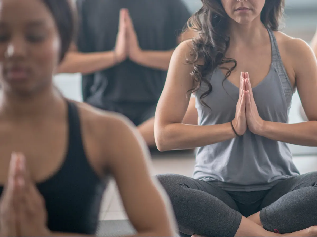 A diverse group of people practicing yoga indoors at a luxury rehab facility, guided by an instructor who demonstrates various individual poses. This serene setting promotes a strong support system for those on their recovery journey from substance use disorder, highlighting the importance of wellness in addiction treatment.