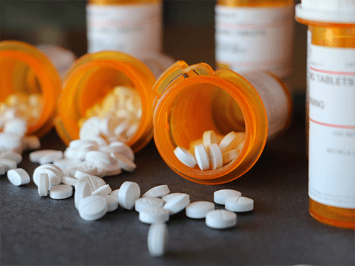 Prescription drugs spilling out of their orange bottle from someone with a prescription pill addiction who needs rehab