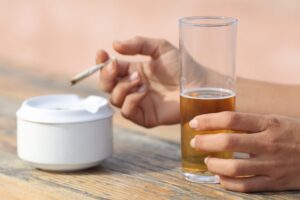 Close-up of a person holding a glass of beer next to an ashtray, used to illustrate the discussion around alcohol withdrawal symptoms and safe detox methods involving Klonopin.