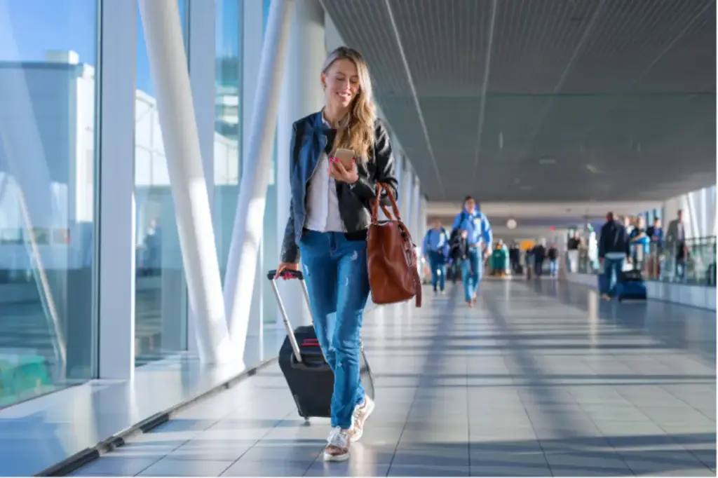 Woman walking through an airport terminal with luggage, preparing to travel for addiction treatment support services.