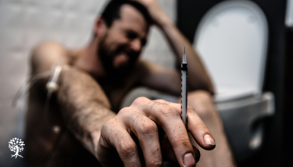 The image depicts a person struggling with a syringe, symbolizing the battle against drug addiction, particularly highlighting the dangers of xylazine addiction and it's lethal fentanyl mixtures that contribute to overdose deaths. This scene reflects the broader issues of illicit drug supply and the urgent need for harm reduction strategies in addressing drug and alcohol dependence.